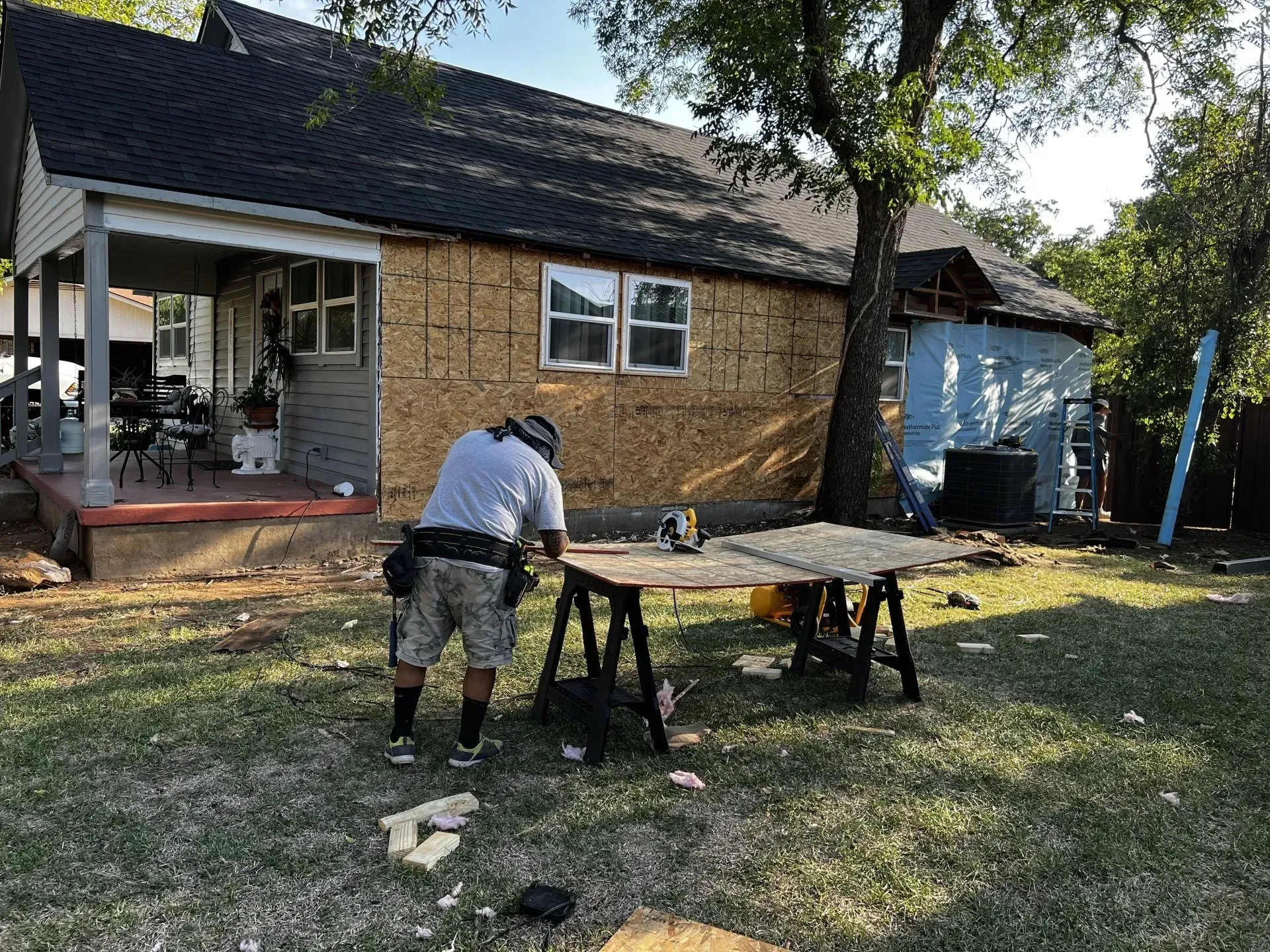 A man is working on a wooden table in front of a house.