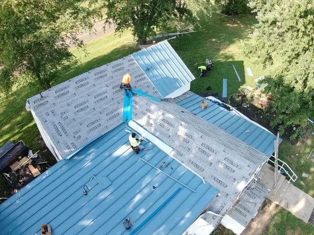 A group of men are working on a blue metal roof.