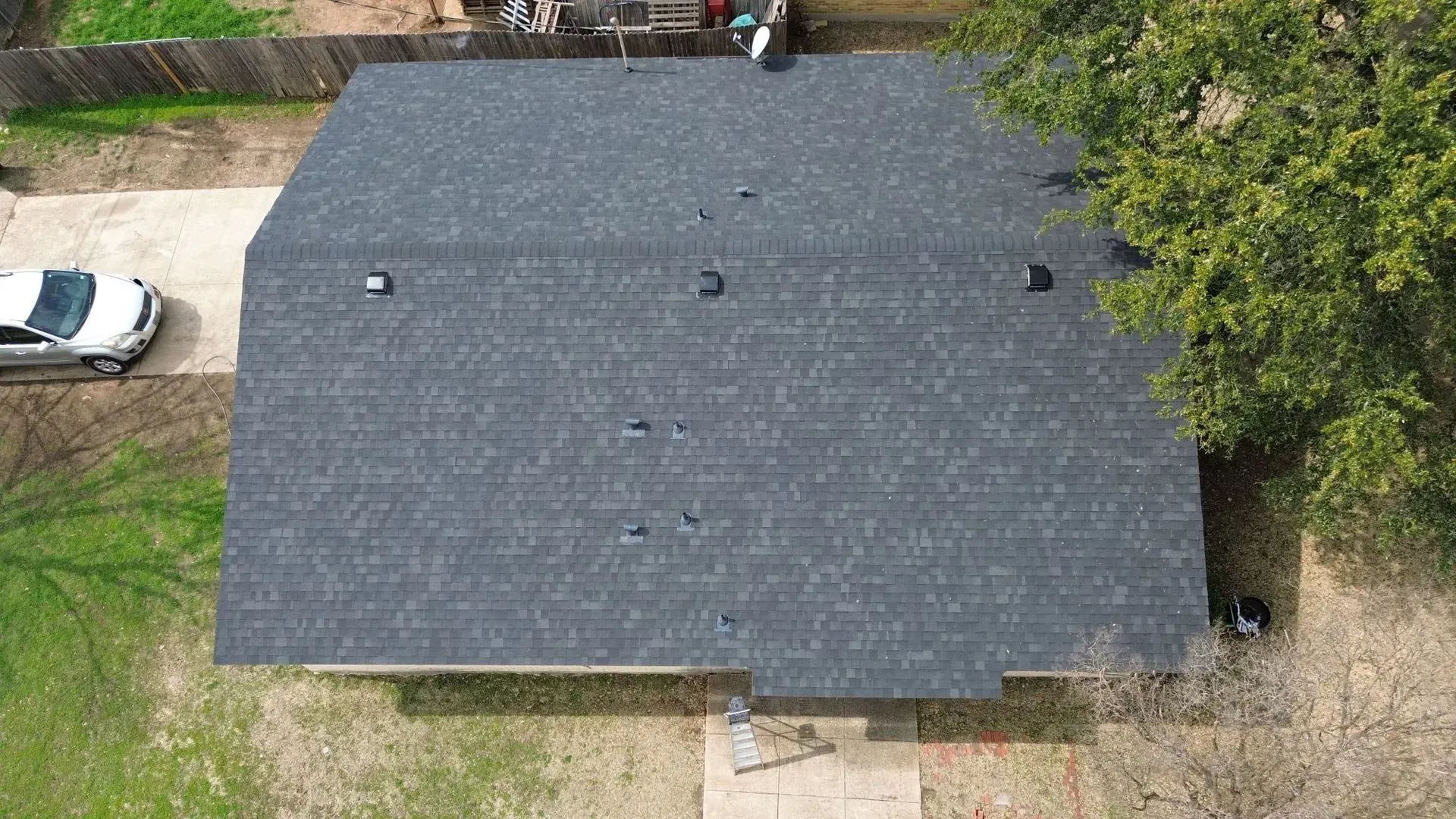 An aerial view of a house with a new roof and a car parked in the driveway.