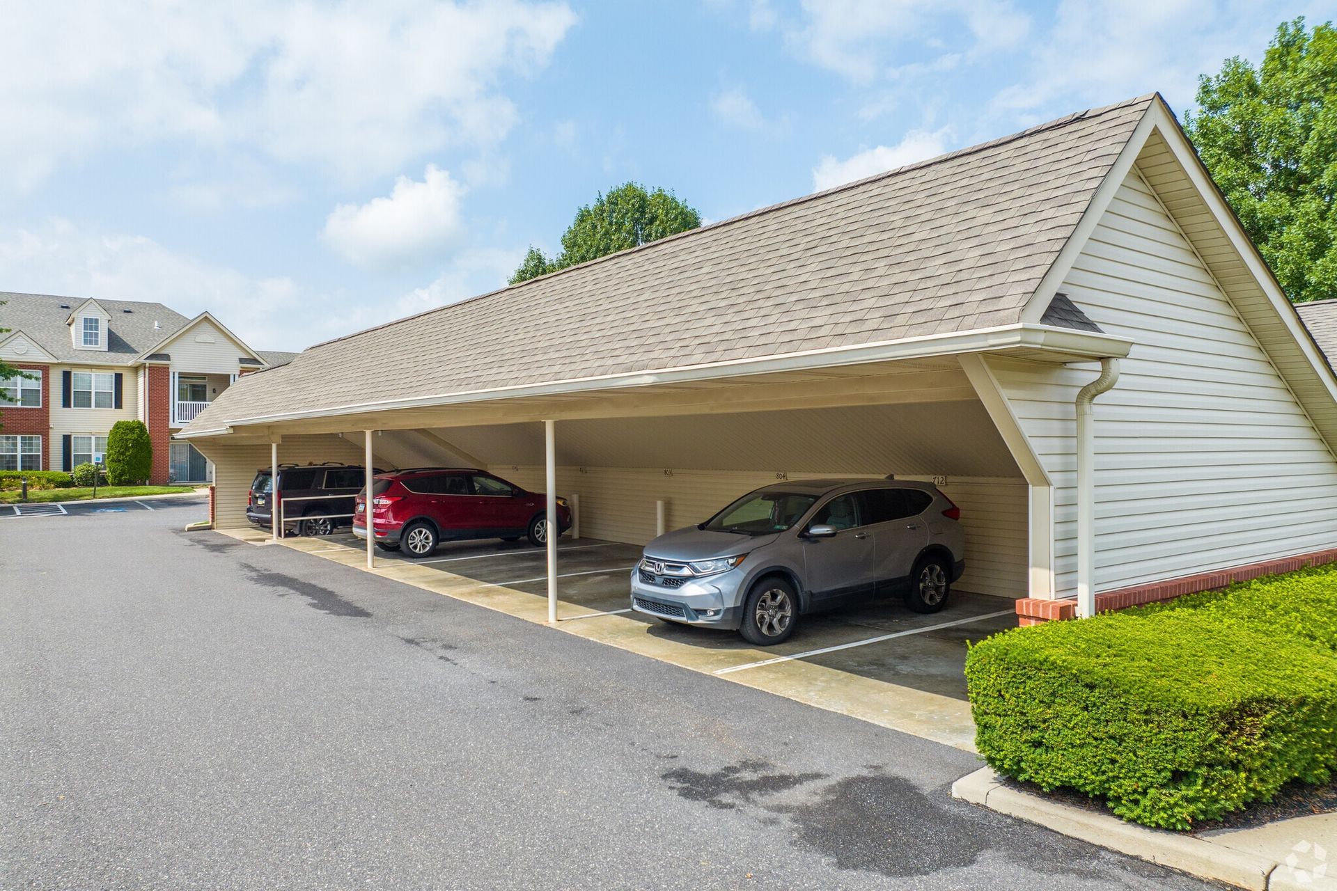 Cars parked under a beige carport structure at an apartment complex on a sunny day.