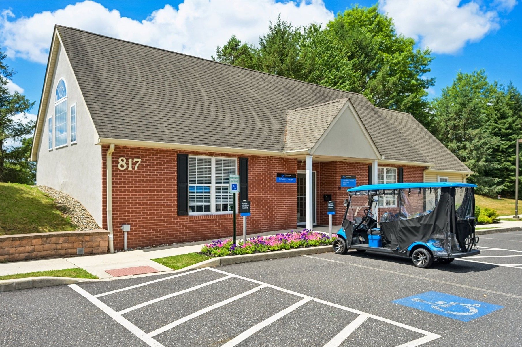 Brick office building with blue door, parking spaces, and a golf cart outside under a bright sky