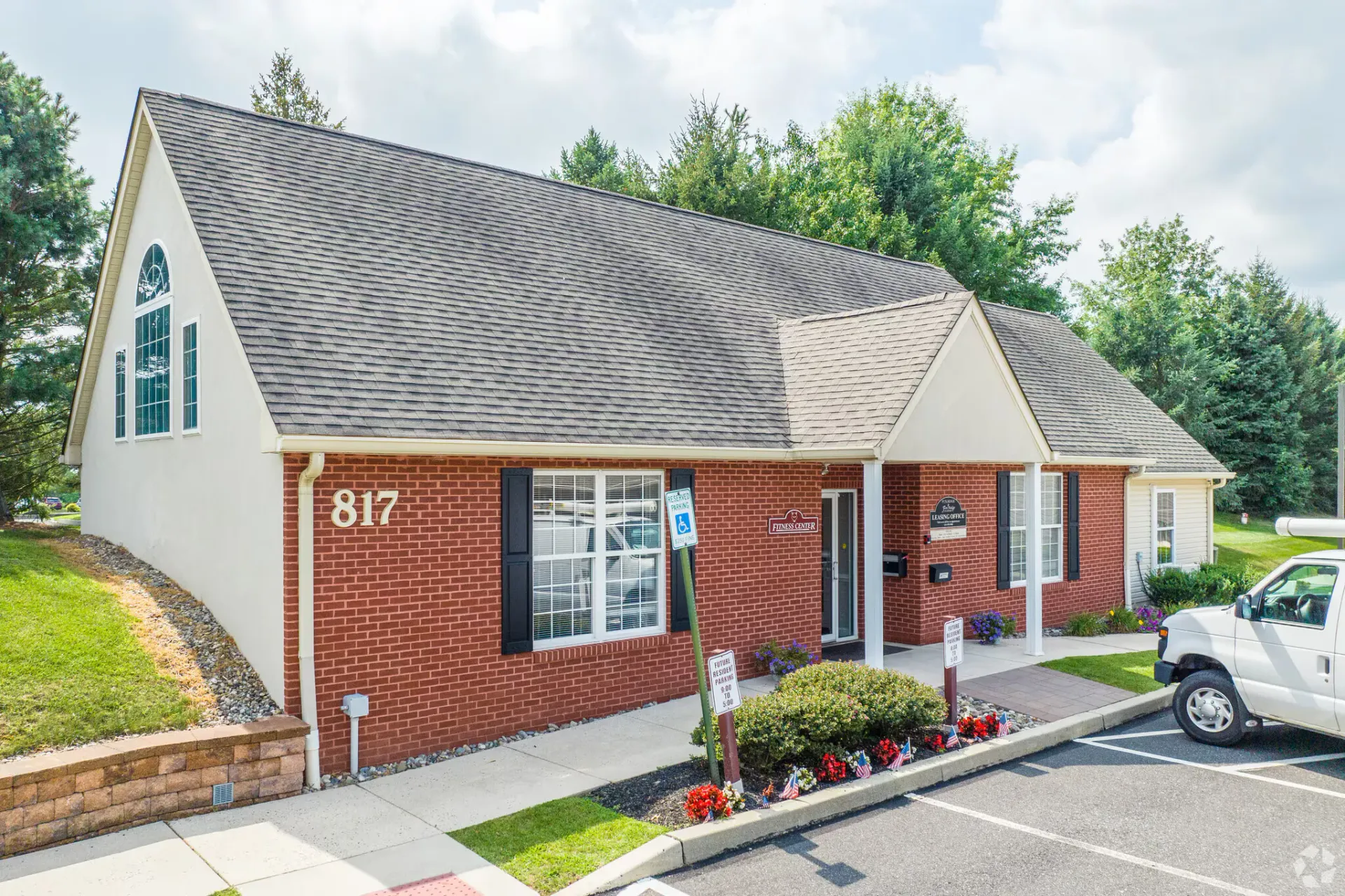Red brick building with gray roof, small flower beds, and a handicap parking sign. Number 817 visible.