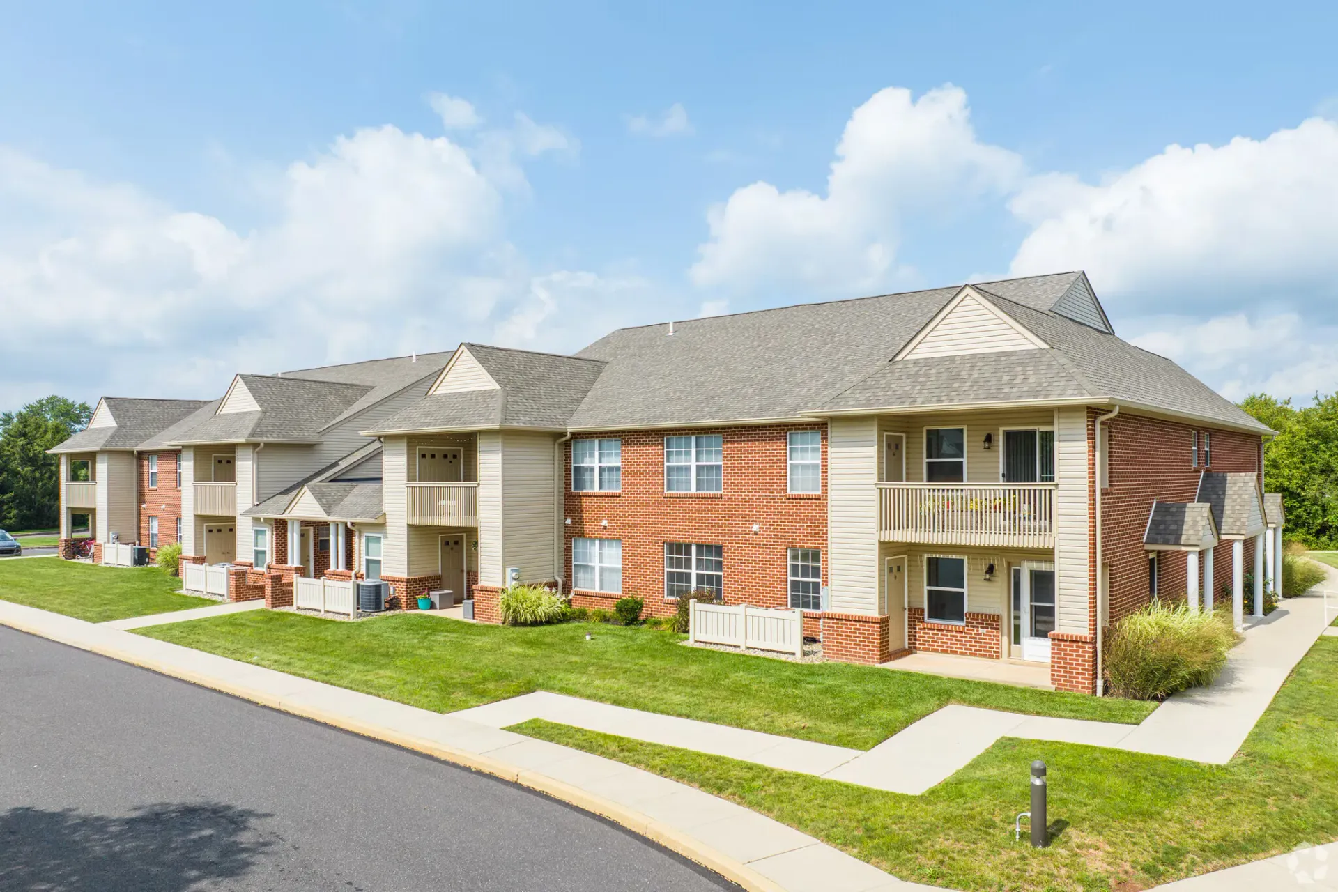 Apartment complex with brick and tan siding, balconies, and green lawn under a partly cloudy sky.