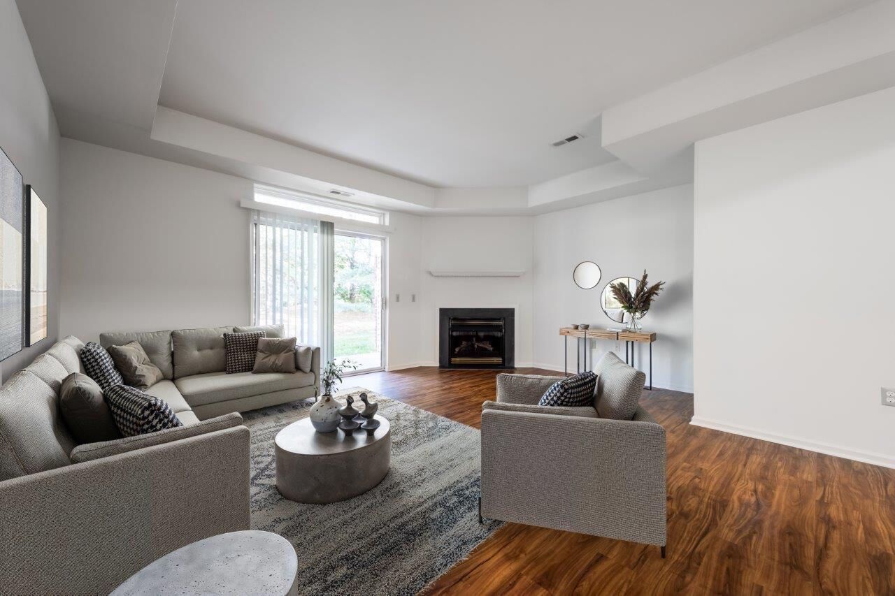 Spacious modern apartment living room with gray sectional, two chairs, fireplace, and sliding glass door. Visit us at Fox Ridge Apartments and view our apartments for rent in Limerick, PA.