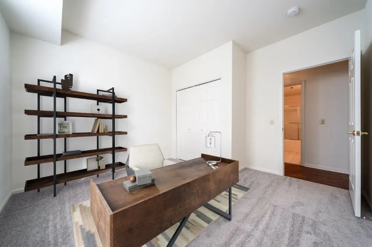 Modern apartment home office with wooden desk, metal shelving, and an open door to a hallway. Visit us at Fox Ridge Apartments and view our pet-friendly apartments for rent in Limerick, PA.