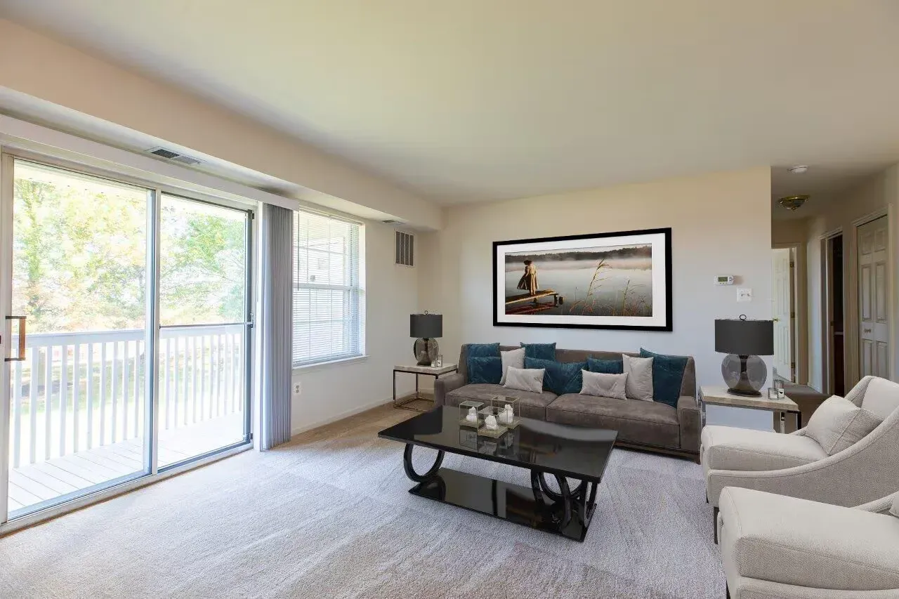 Bright living room in an apartment with a gray sofa, glass coffee table, and sliding balcony doors. Visit us at Fox Ridge Apartments and view our modern, garden-style 1 and 2 bedroom apartments in Limerick, PA.