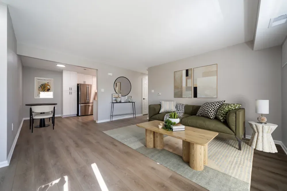 Modern apartment living room with olive sofa, wood coffee table, and kitchen in the background. Visit us at Fox Ridge Apartments and view our apartments for rent in Limerick, PA.
