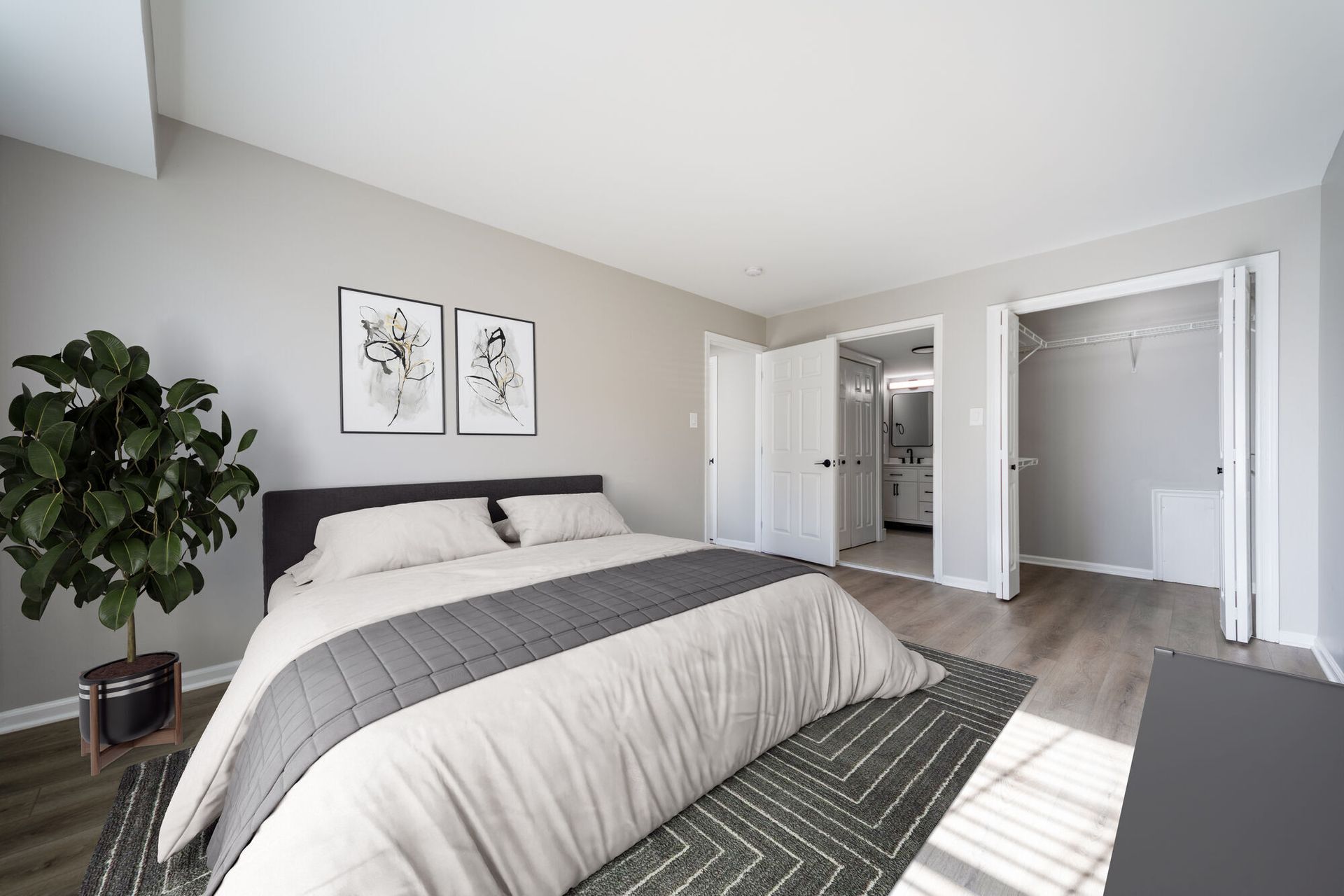 Bedroom with a large bed, neutral gray walls, and an open closet near the bathroom. Visit us at Fox Ridge Apartments and view our modern, garden-style 1 and 2 bedroom apartments in Limerick, PA.