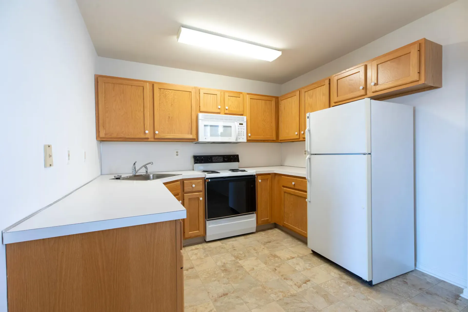 Bright kitchen in an apartment with wood cabinets, white refrigerator, stove, microwave, and sink. Visit us at Fox Ridge Apartments and view our pet-friendly apartments for rent in Limerick, PA.