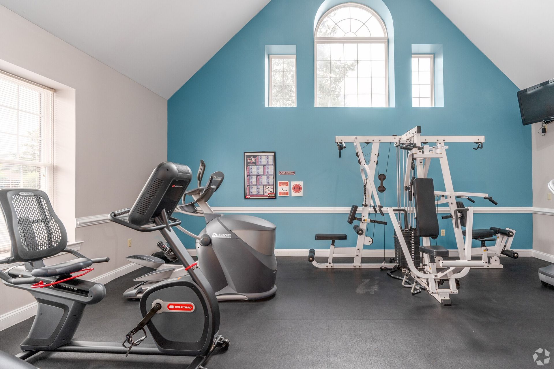 Gym interior with exercise equipment against blue wall, natural light.