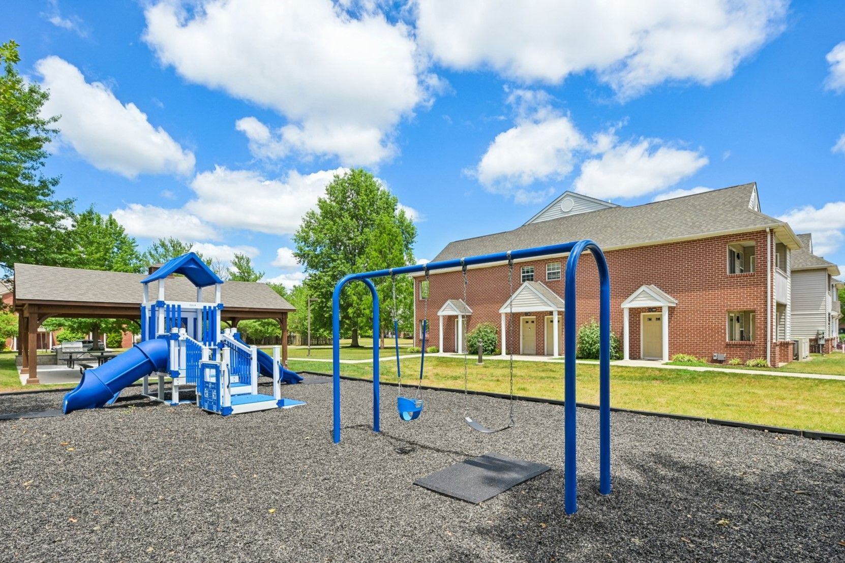Playground with blue swings and slide beside a brick building under a bright cloudy sky