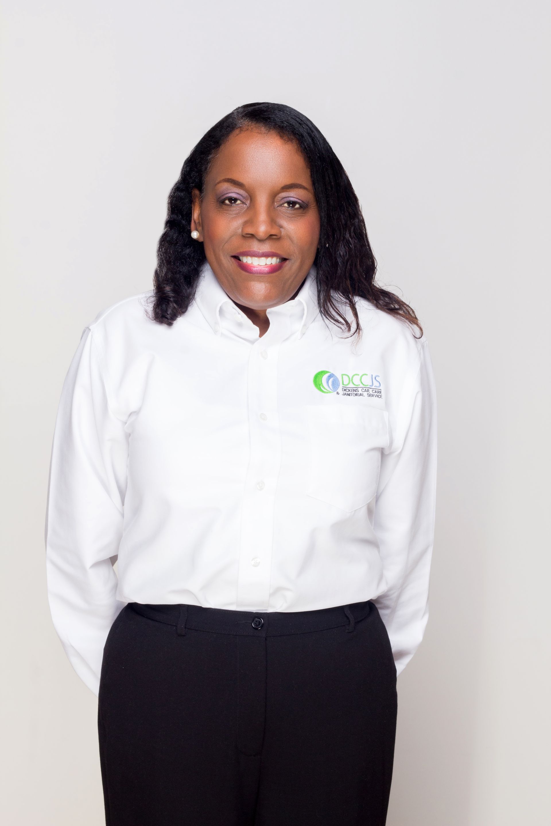 A woman wearing a white shirt and black pants is smiling for the camera.