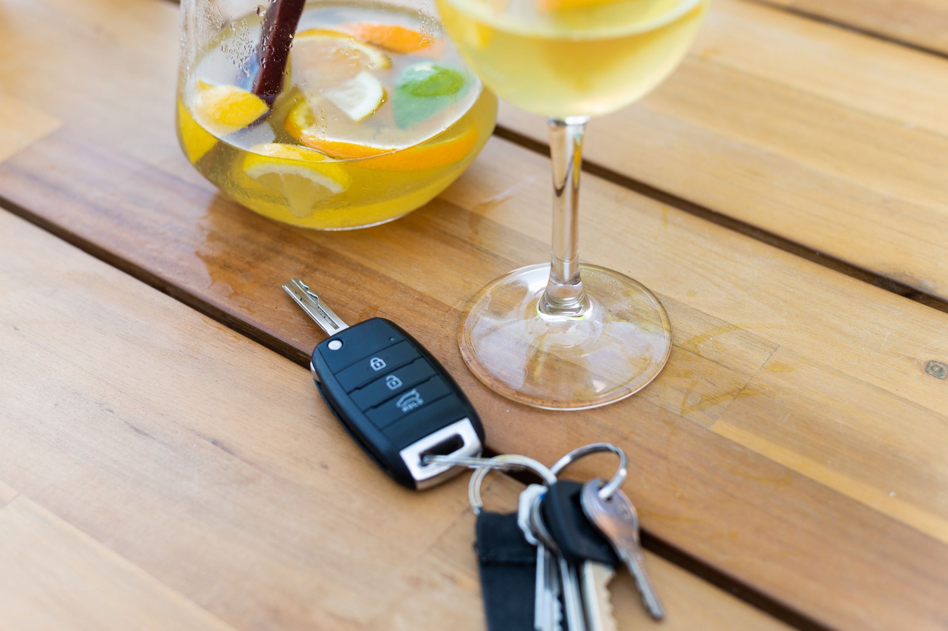 Close-up photo of an upper part of a wooden table with the keys of a car and a glass of sangria