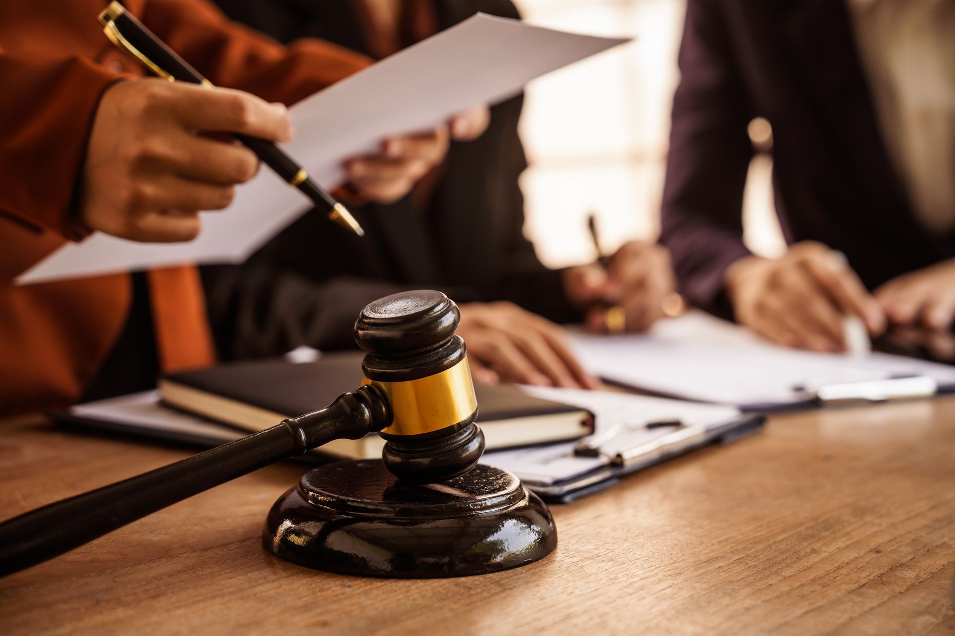 Judge’s gavel sits on a desk as people review and sign legal documents. Judge’s gavel sits on a desk as people review and sign legal documents.