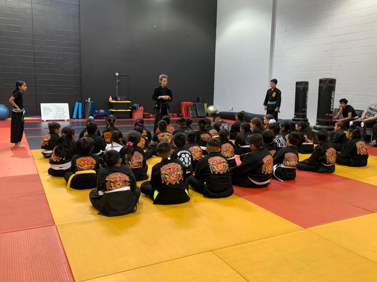 A group of children are sitting on the floor in a gym.