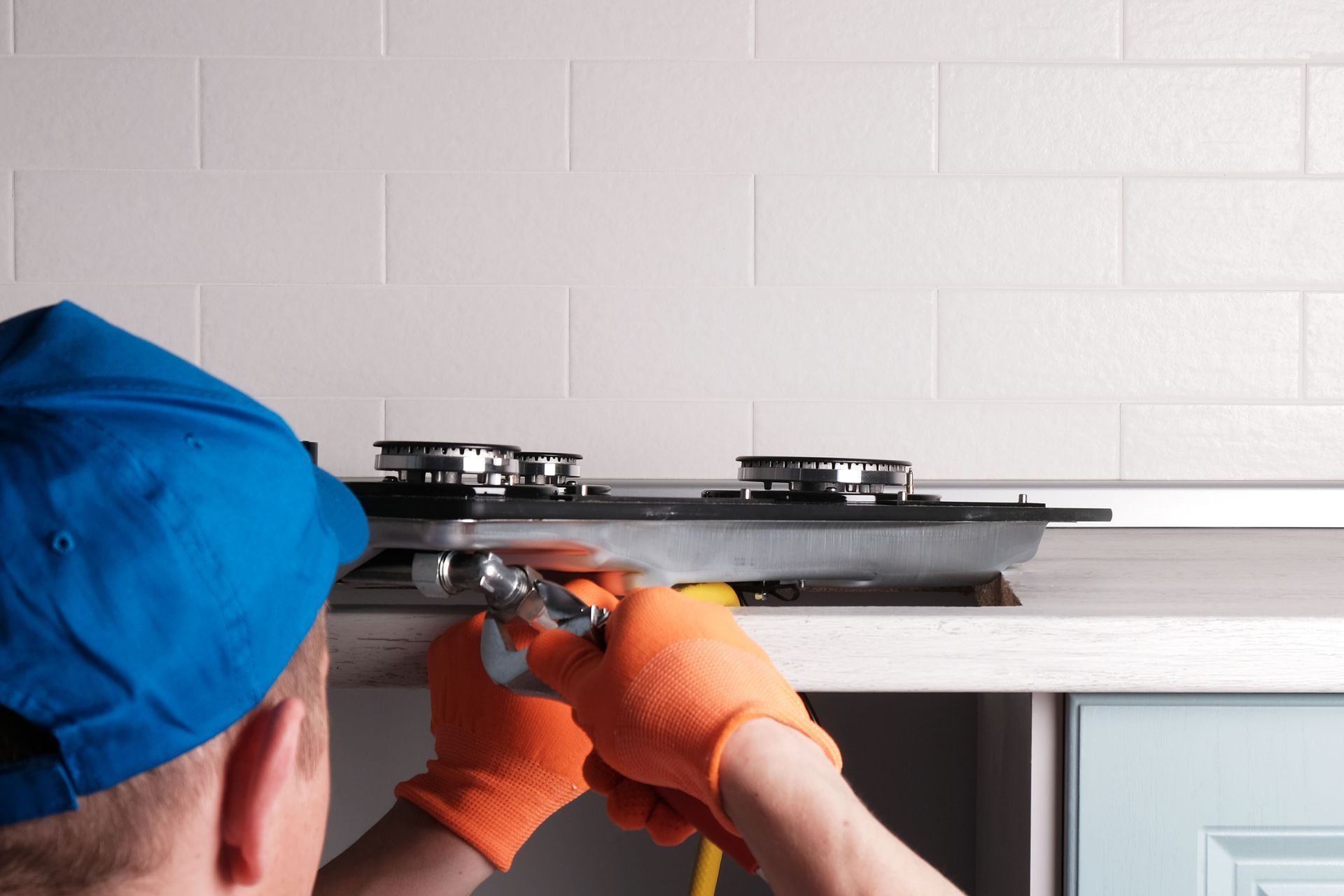 Image shows a plumber working on the gas join on the base of a gas stove.