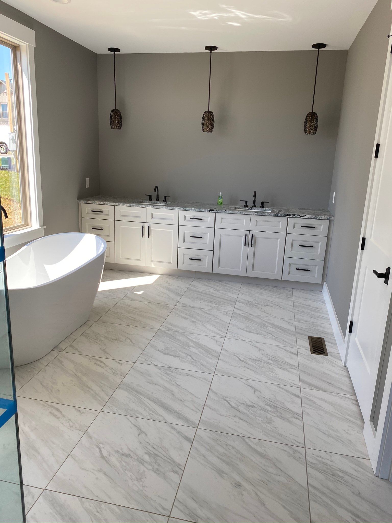 A bathroom with a tub , sinks , cabinets and a window.