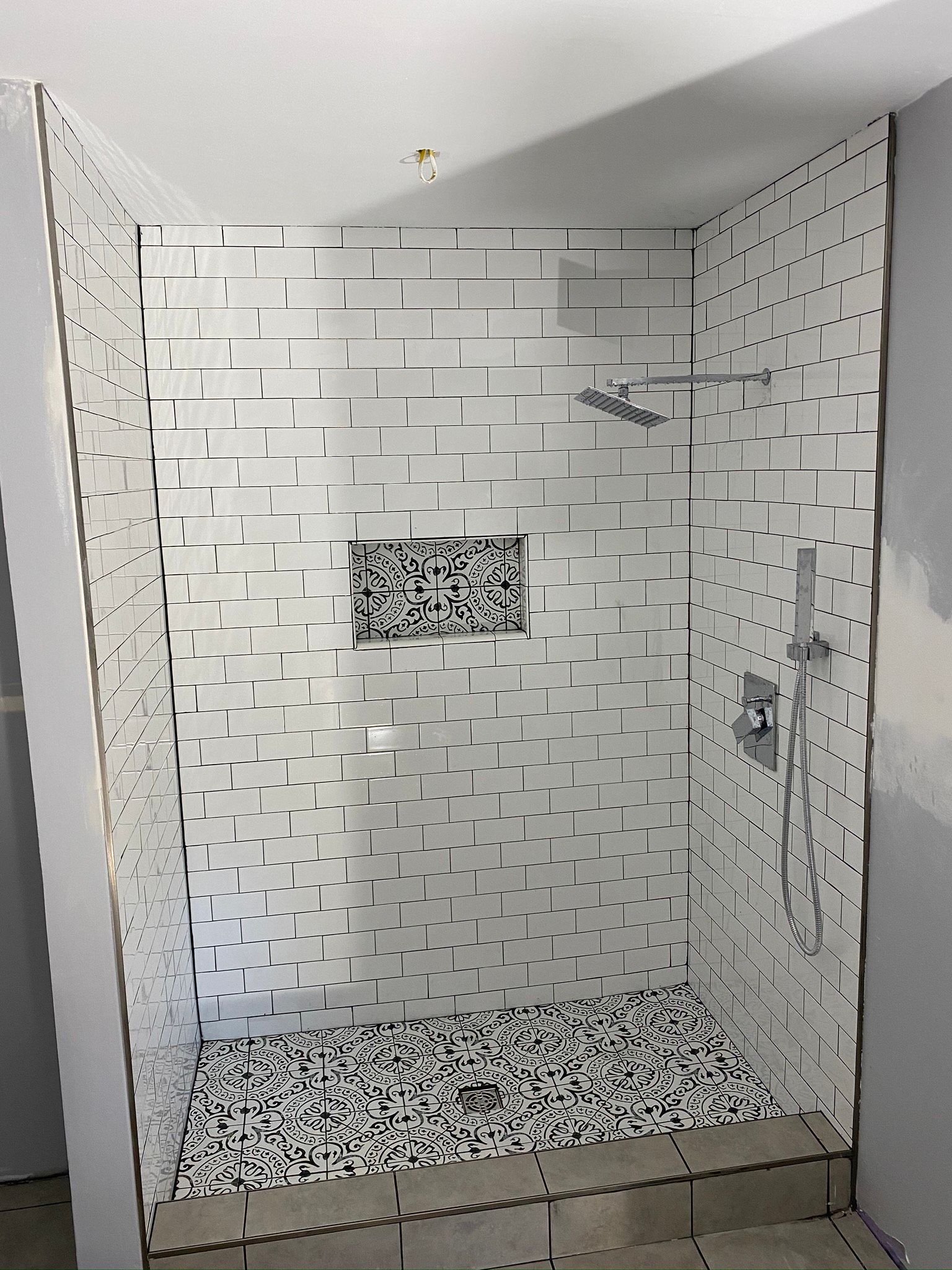 A walk in shower with white tiles and a mosaic floor