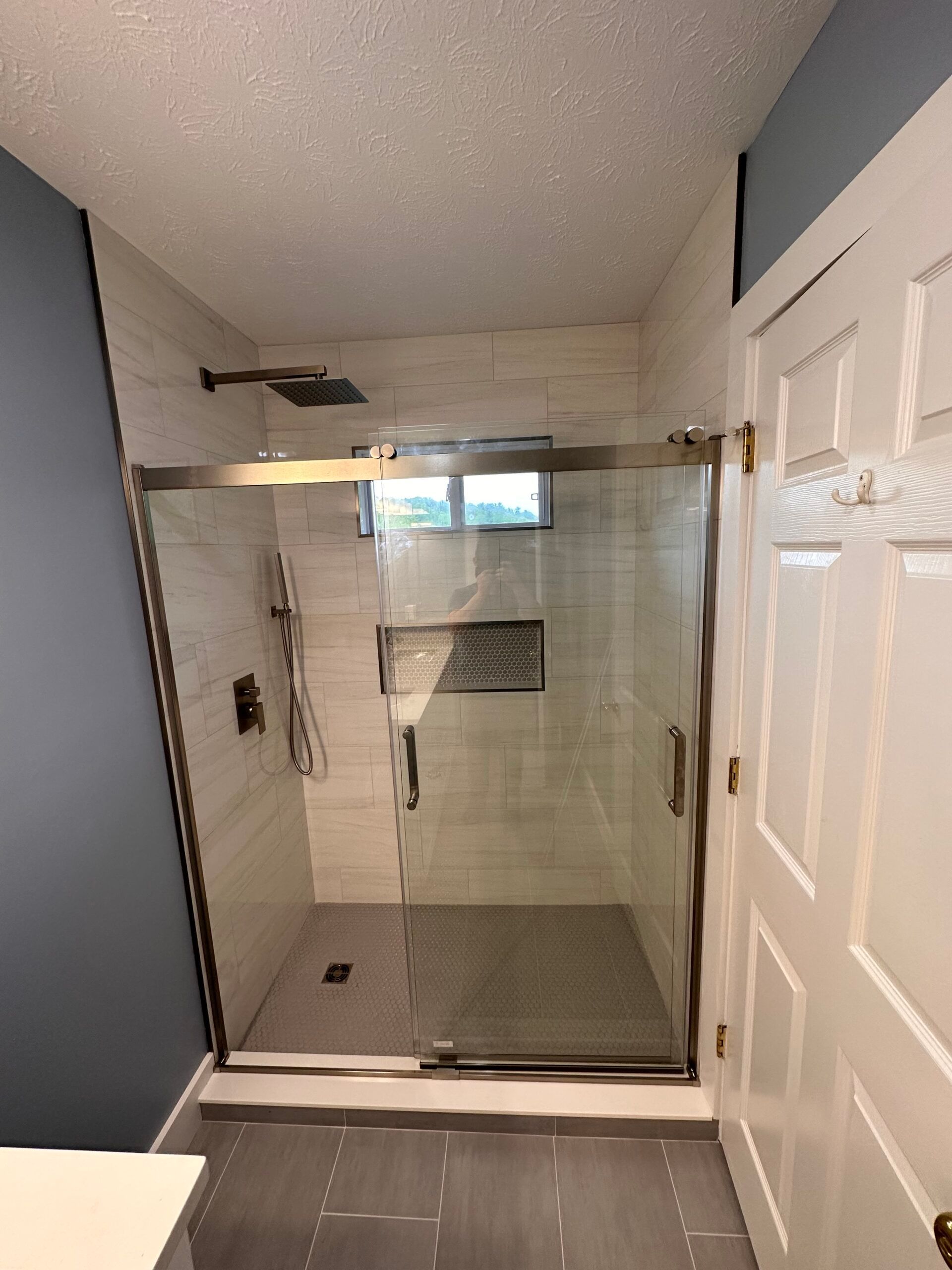A bathroom with a sliding glass shower door and a window.