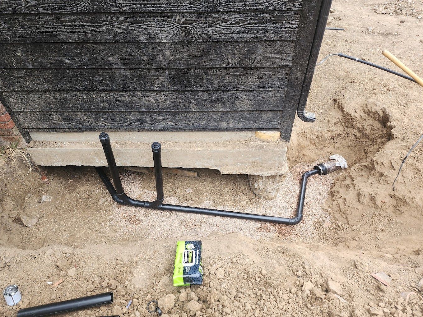 Black metal gas pipes near a building, in a dirt setting. Level nearby.