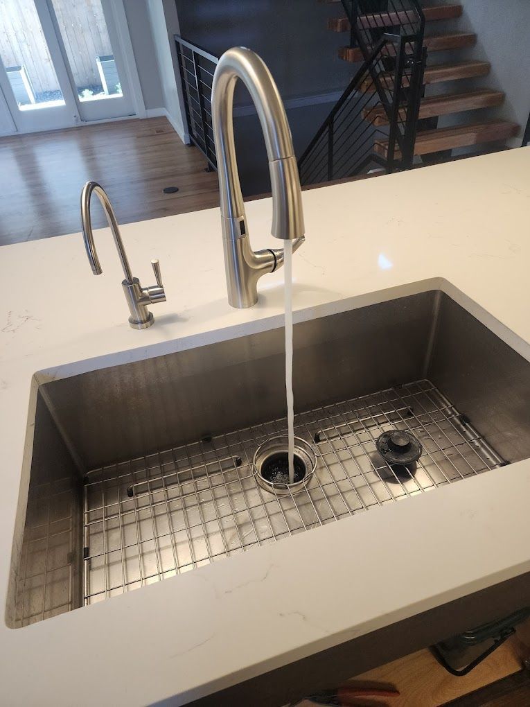 Stainless steel sink with running water, two faucets on a white countertop.