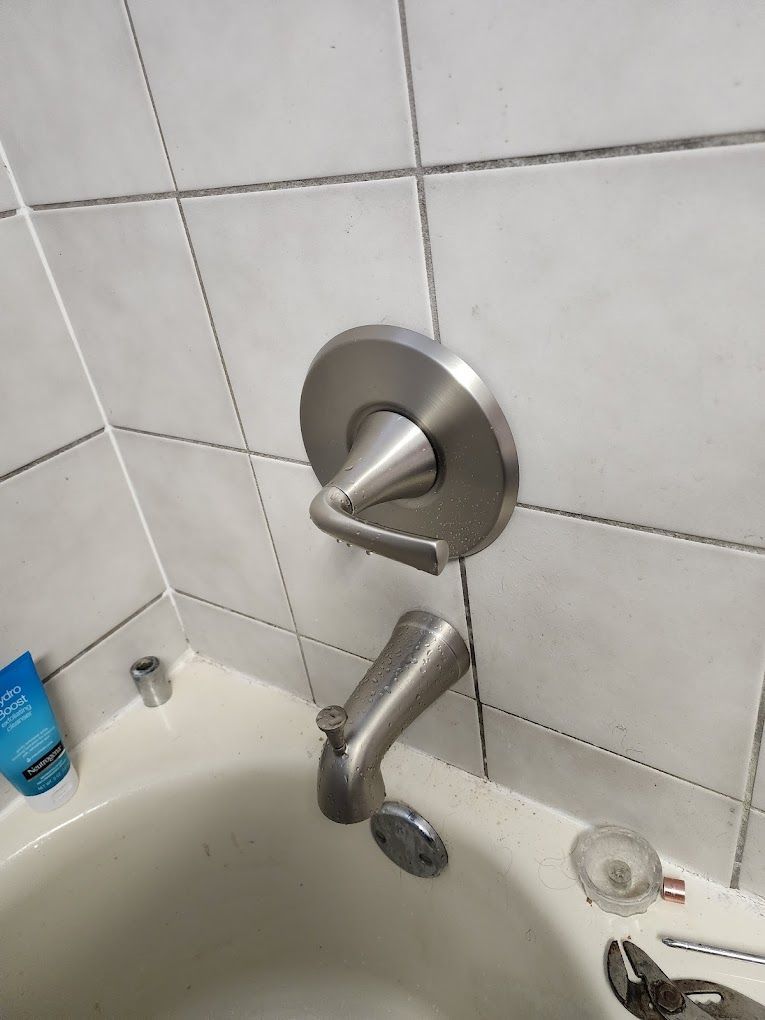 A silver bathtub faucet and handle on a white-tiled wall in a bathroom.