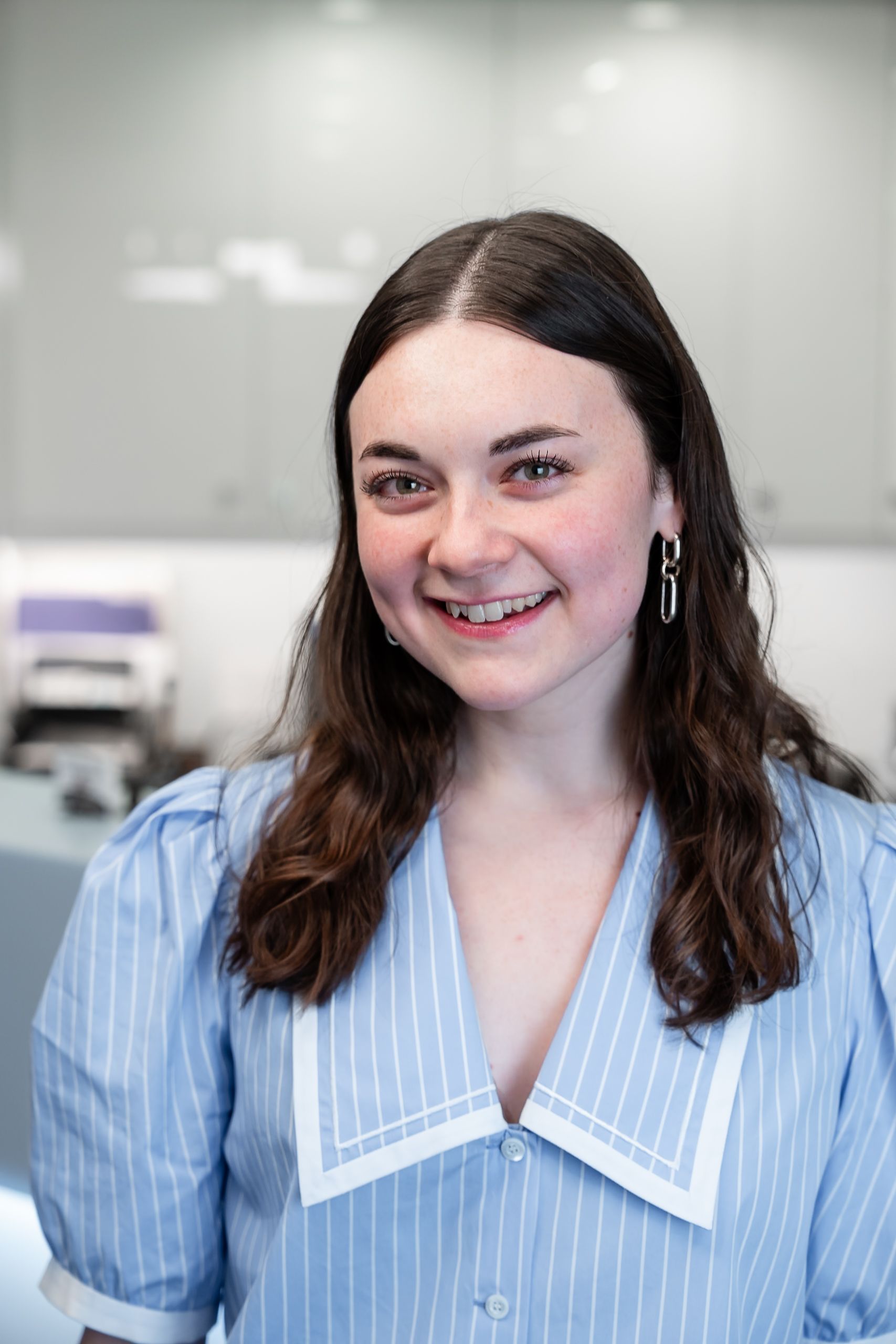 Woman in red sweater, smiling, leaning on a counter, near a window and printer.