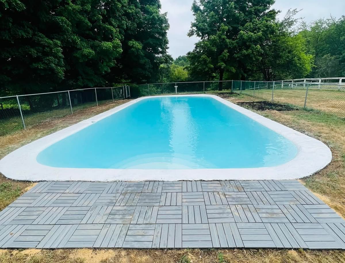 A large swimming pool is surrounded by trees and a fence