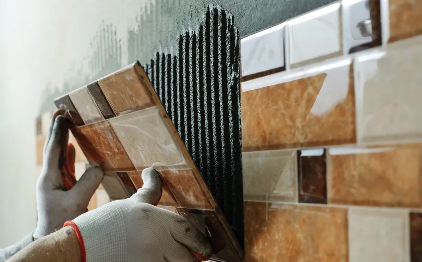 Tiler placing ceramic wall tile in position over adhesive