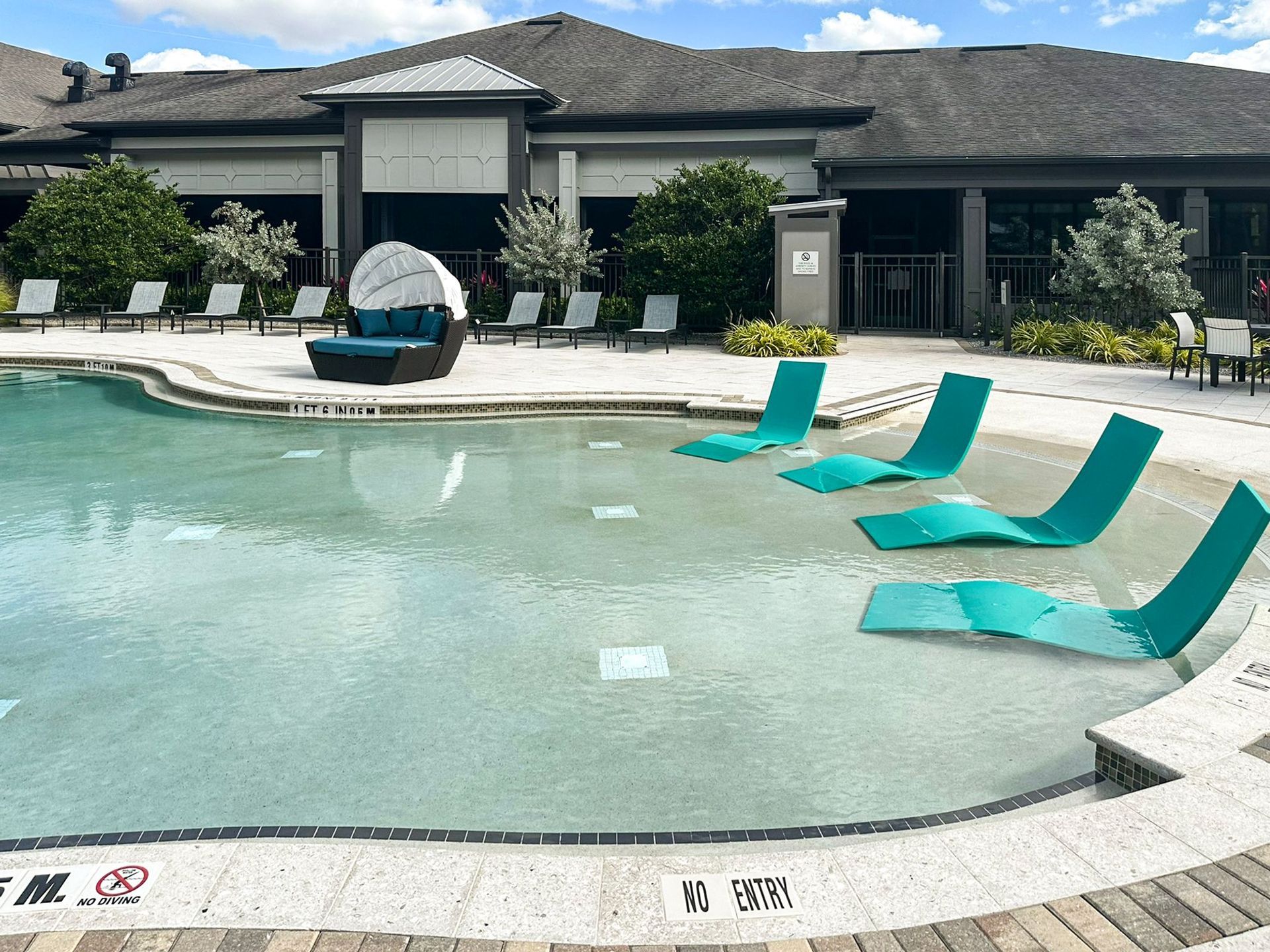beach-entry swimming pool with teal lounge chairs on the tanning deck