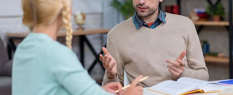 A man and a woman are sitting at a table talking to each other.