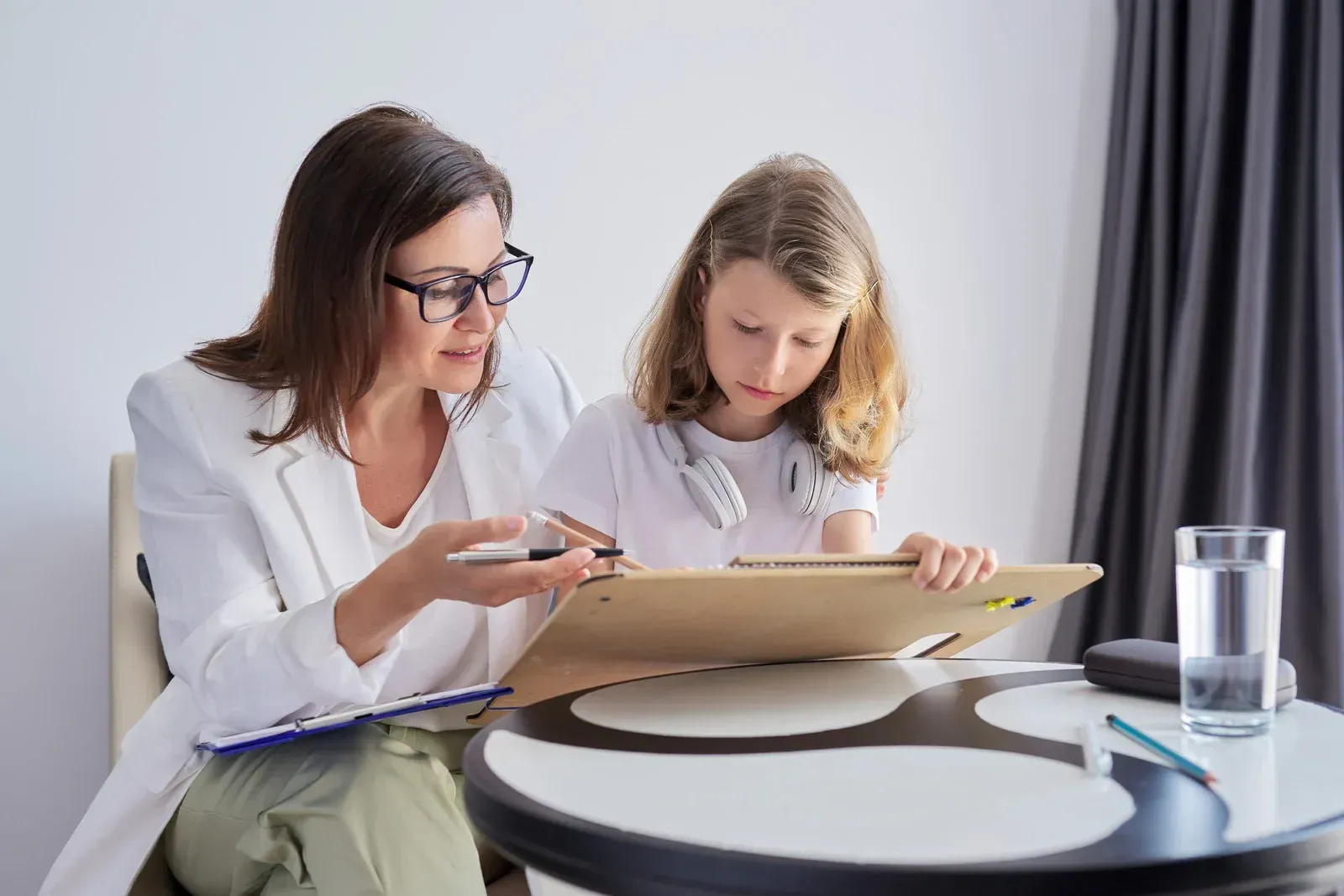 A woman and a girl are sitting at a table looking at a clipboard.