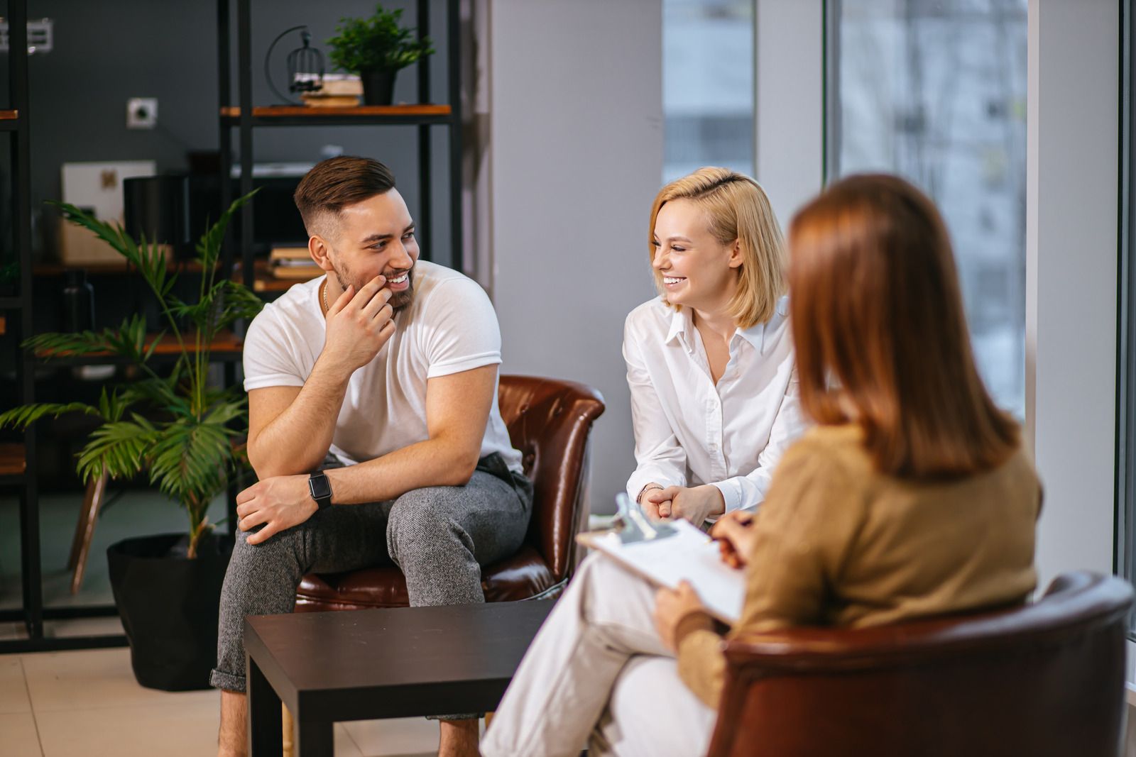 A man and a woman are sitting in chairs talking to a woman.