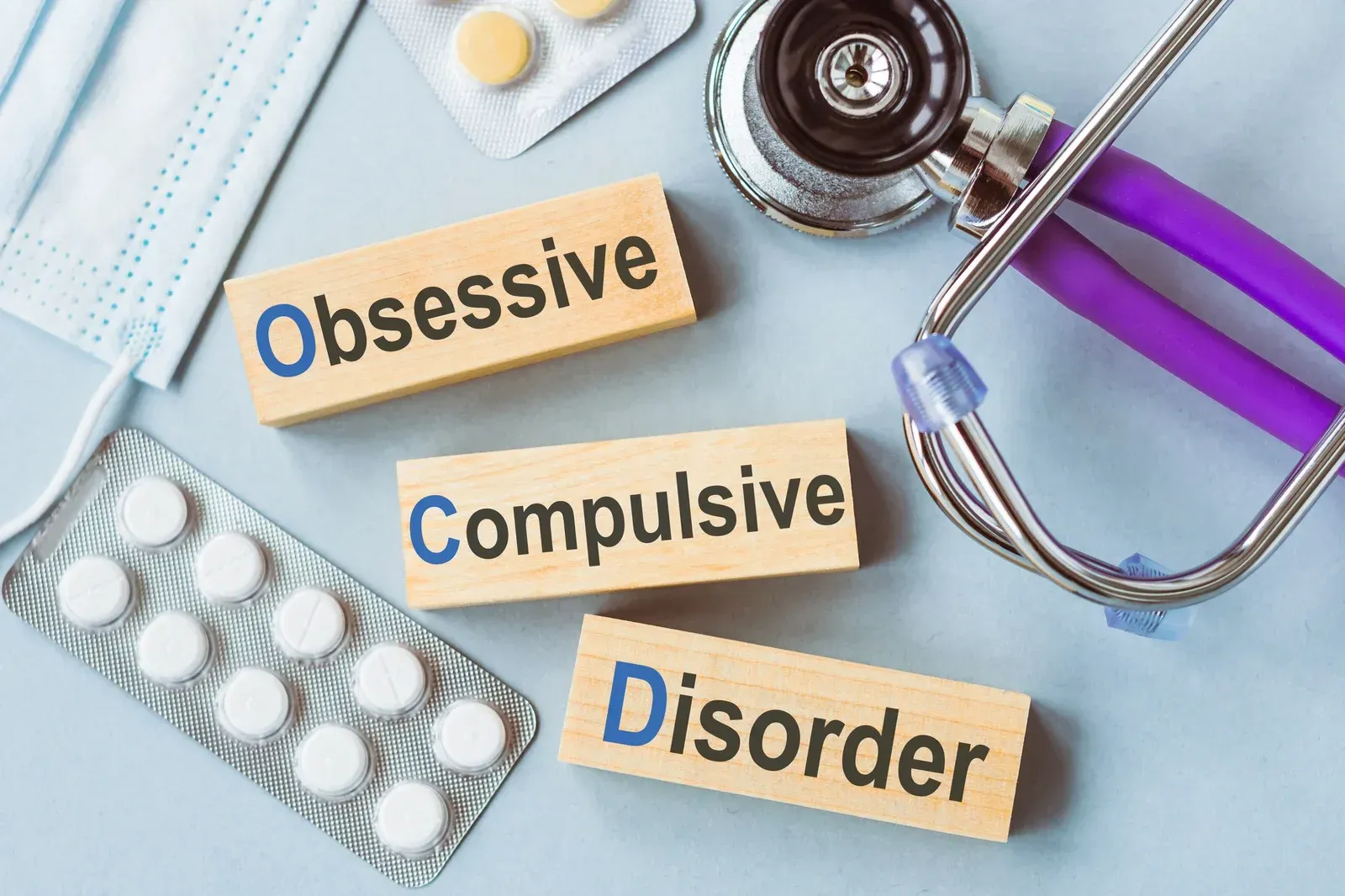 The word obsessive is on a wooden block next to a stethoscope and pills.