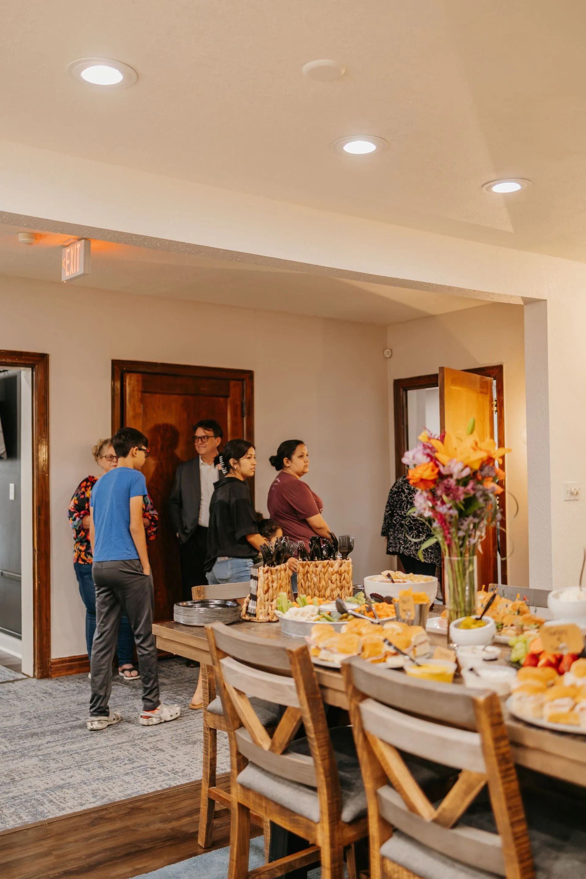 A group of people are standing around a table with food on it.