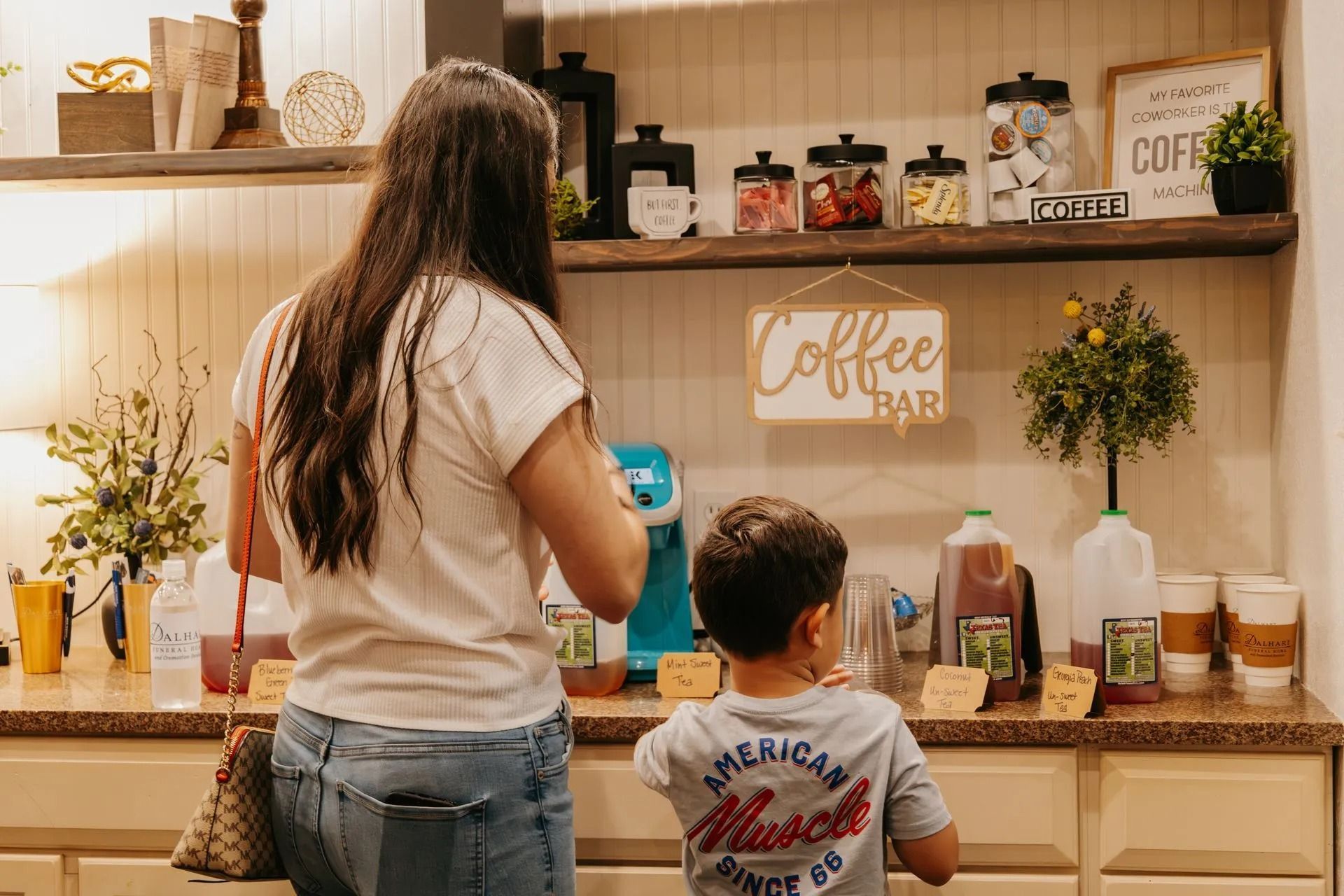 A woman and a child are standing in a kitchen in front of a coffee bar.