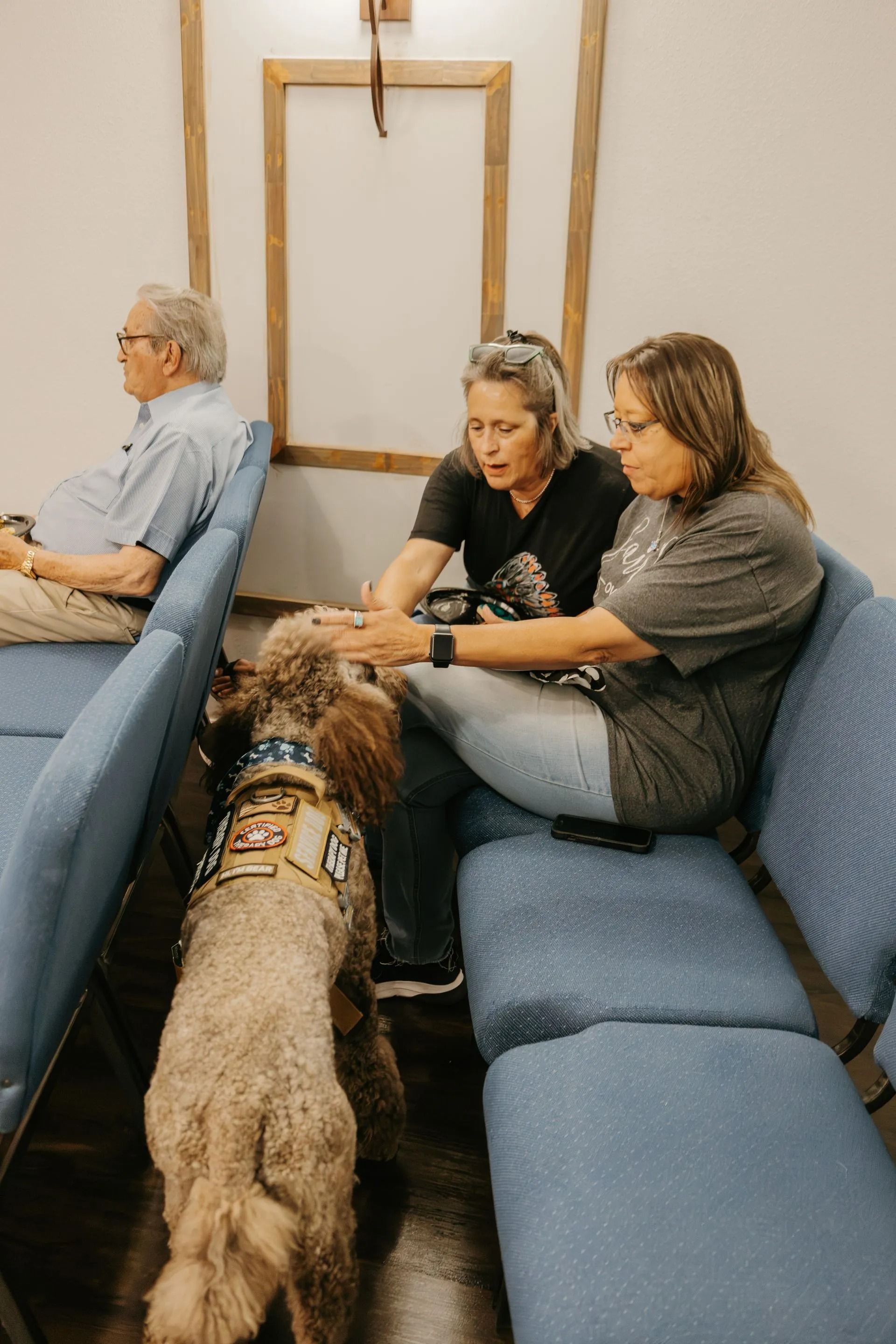 Two women are sitting on a couch with a dog in a waiting room.