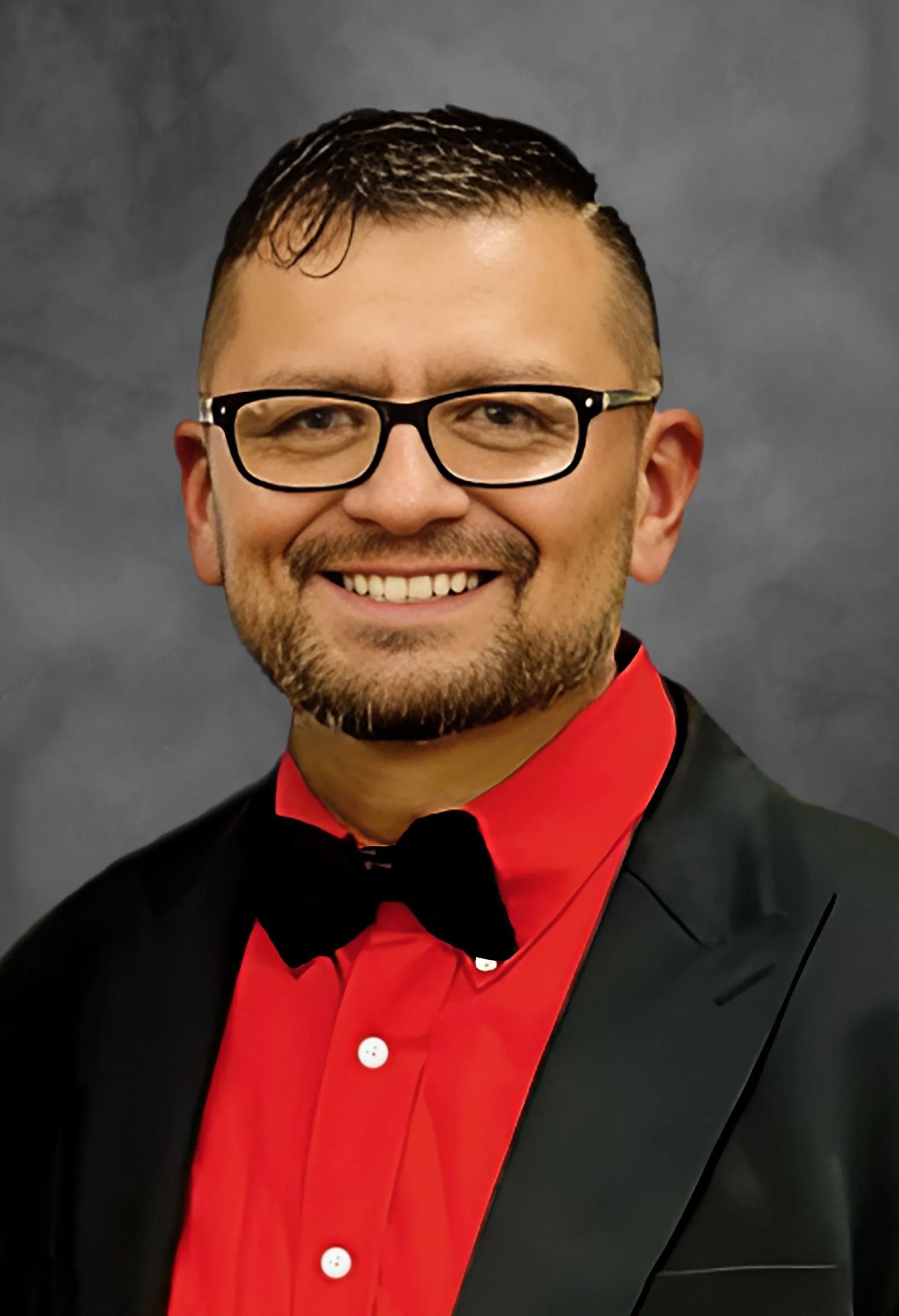 A man wearing glasses and a red shirt is smiling for the camera.