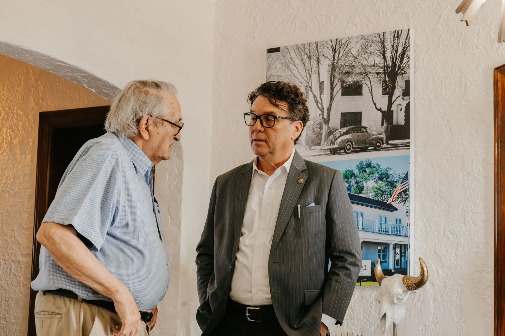 Two men are standing next to each other in a room talking.