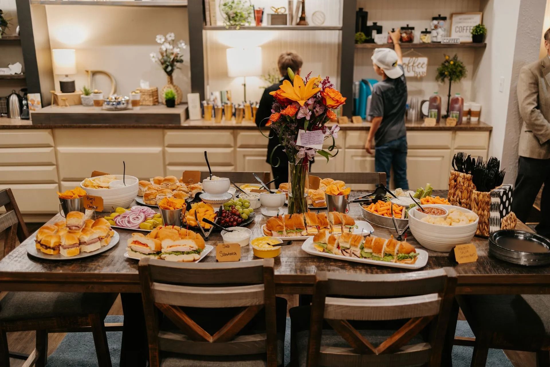 A table with a lot of food on it and people standing around it.