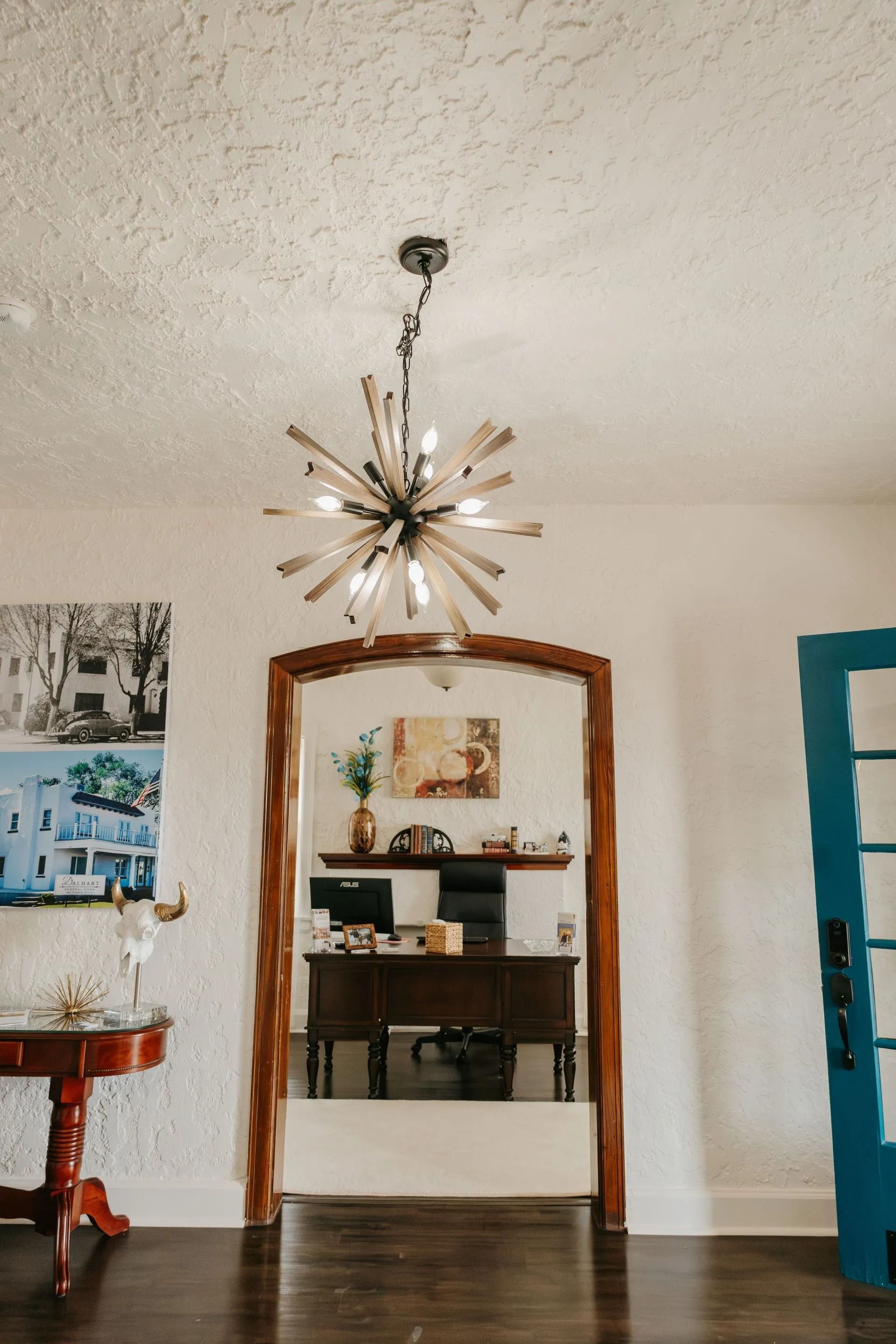 A living room with a desk and a chandelier hanging from the ceiling.