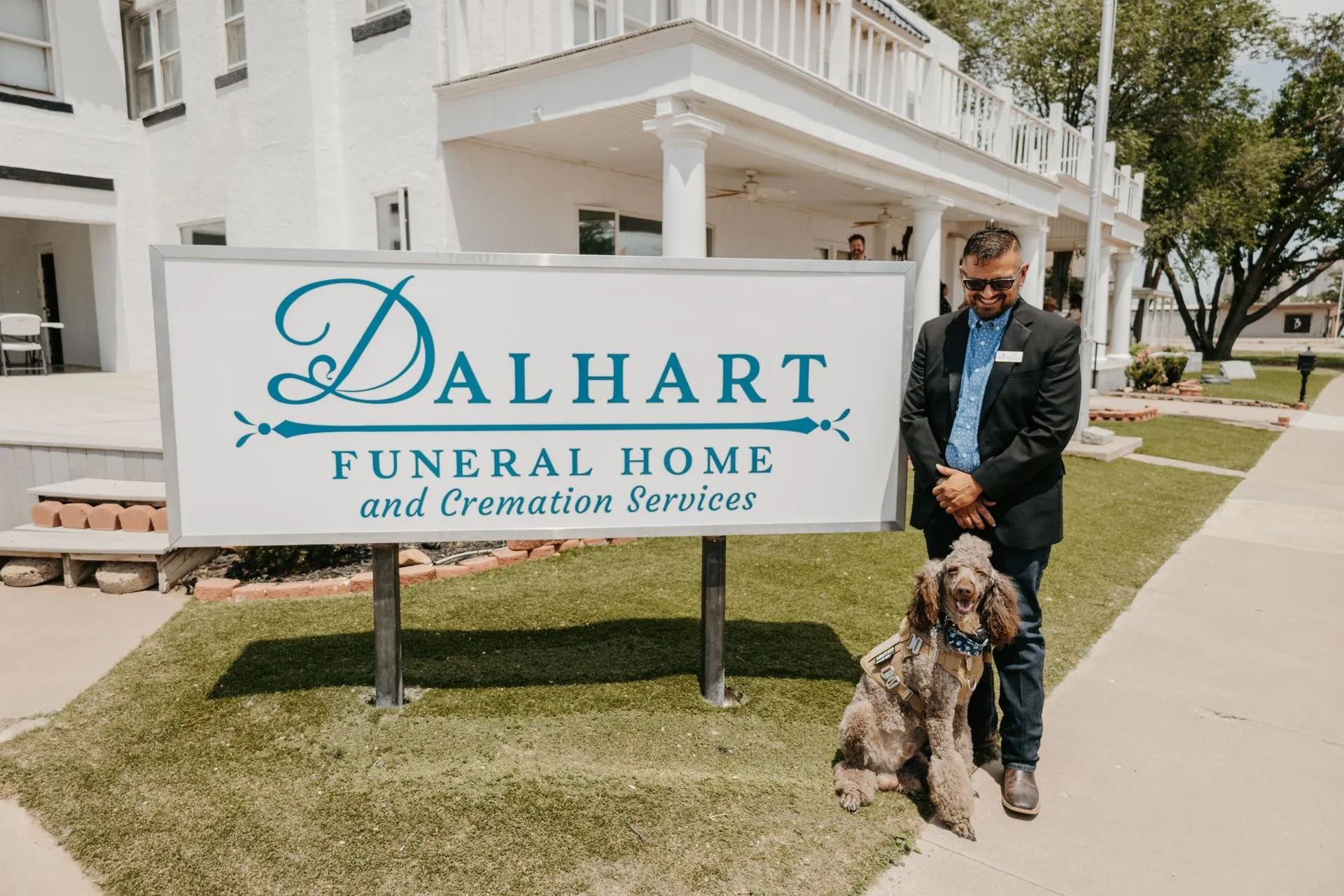 A man standing next to a dog in front of a dalhart funeral home and cremation services sign.