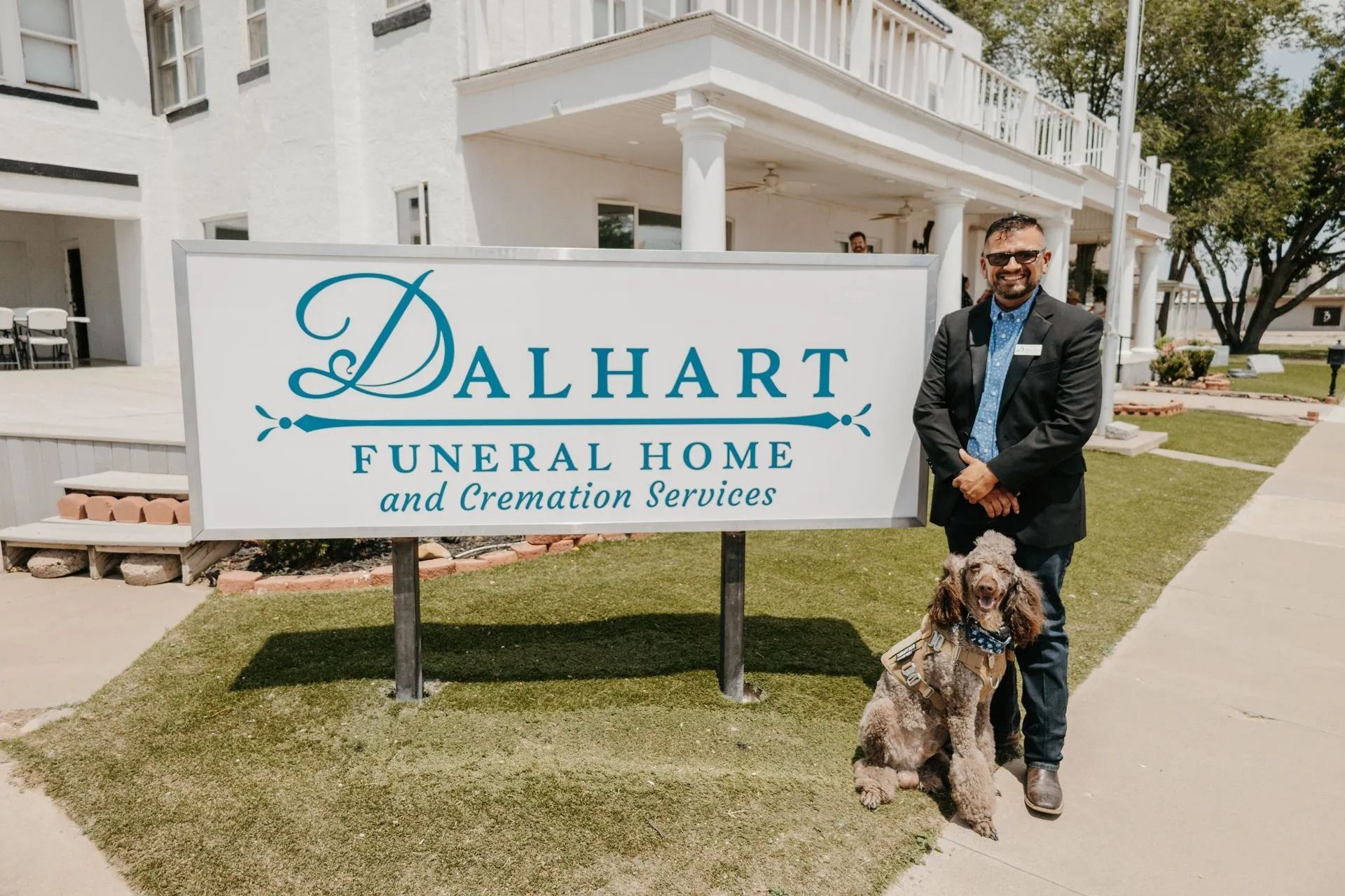 A man and a dog are standing in front of a sign for dalhart funeral home and cremation services.