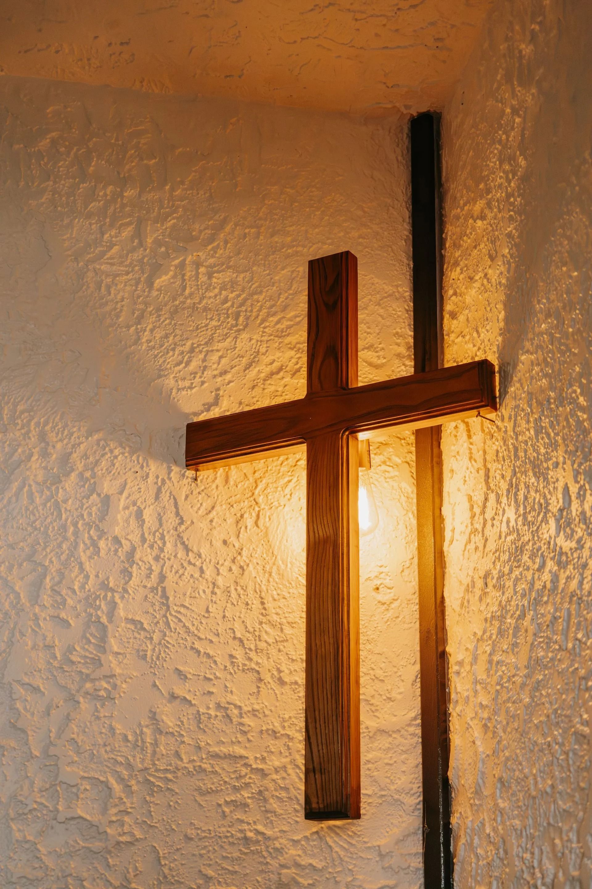 A wooden cross is hanging on a white wall in a church.