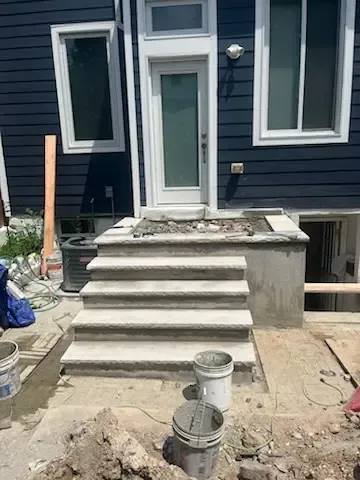 Front steps of a house under construction, with fresh concrete stairs, tools, and buckets in the foreground