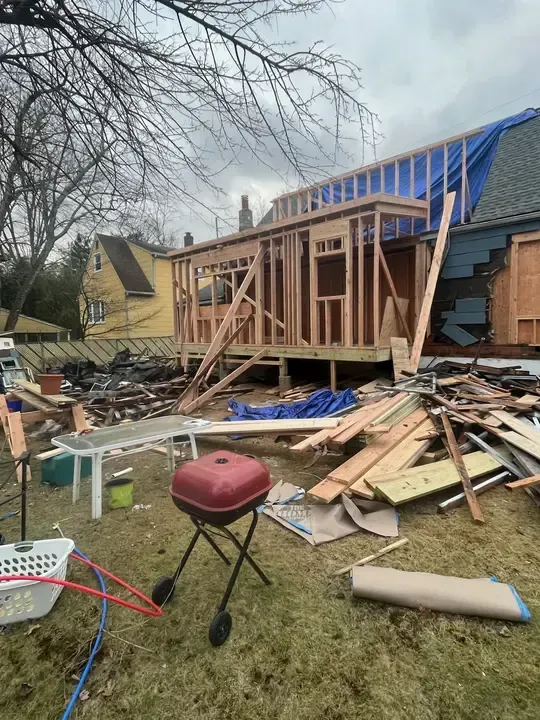 House under construction with roof damage, collapsed debris, and exposed wooden framing in a yard