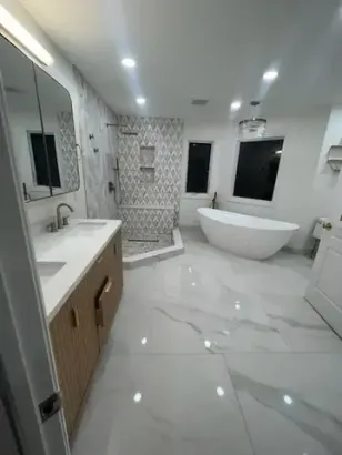 Modern white bathroom with marble floor, glass shower, vanity, and freestanding tub