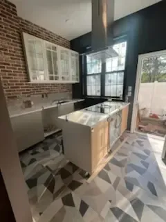 Bright kitchen with brick wall, white cabinets, island, and patterned tile floor in sunlight