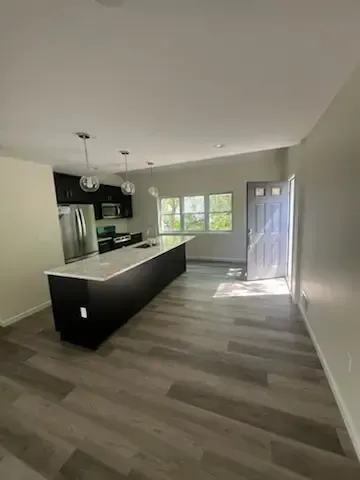 Empty modern kitchen and dining area with black island, light wood floors, and sunlight through windows