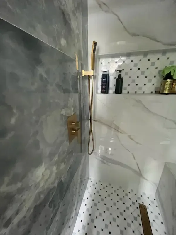 Modern shower stall with gray tile, white marble walls, black fixtures, and mosaic floor tiles